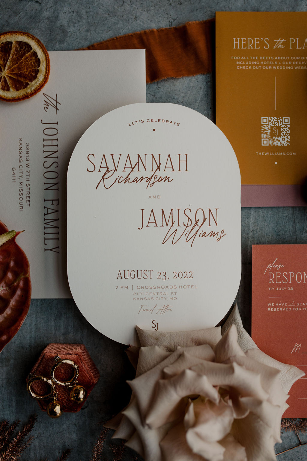 Wedding stationery flat lay with the focus on a boho, oval-shaped invitation card with florals and fruit all around it.
